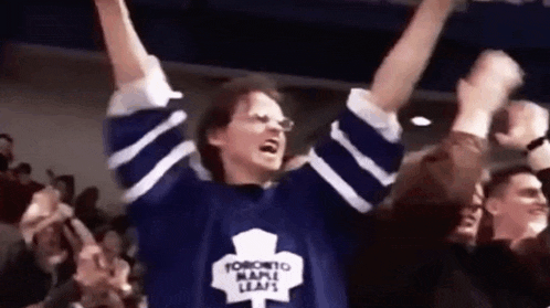 a man wearing a toronto maple leafs jersey is raising his arms in the air