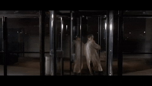 a man in a white coat is standing in a revolving doorway .