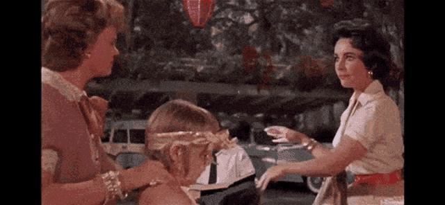 three women are standing next to each other talking to a little girl wearing a gold headband .