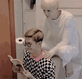 a man is sitting on a toilet next to another man who is holding a book .