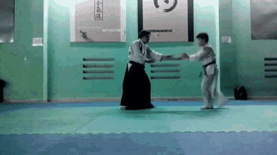 two men are practicing martial arts in a gym and one of them is wearing a black belt .