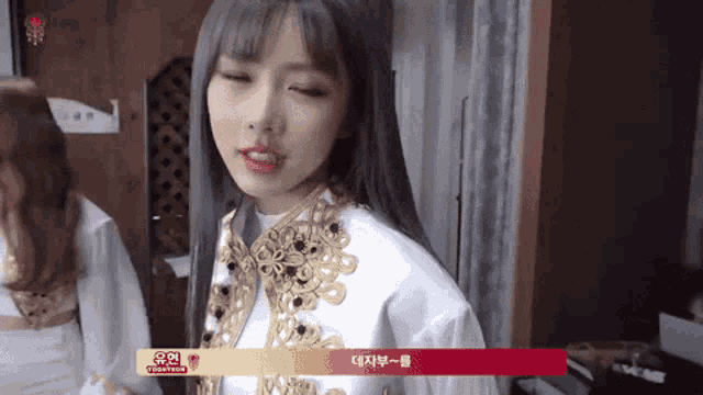 a girl with long hair is wearing a white jacket with gold embroidery
