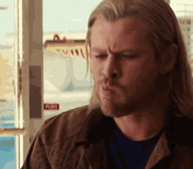 a man with long hair and a beard is making a face in front of a window .