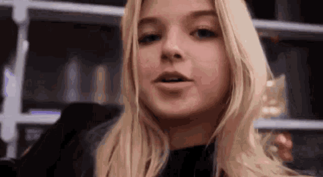 a young woman with blonde hair is making a funny face in front of a bookshelf .