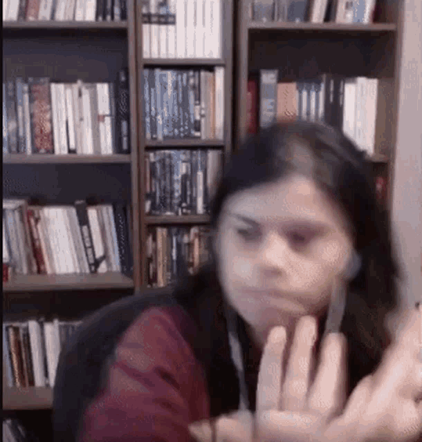 a woman is sitting in front of a bookshelf holding a knife to her face .