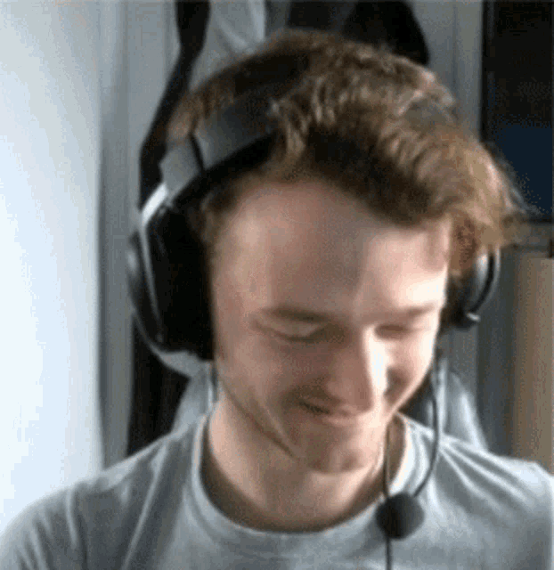 a man wearing headphones and a microphone is smiling and looking down .
