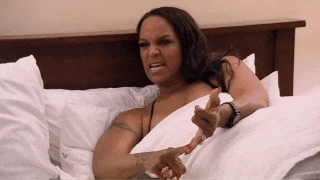 a woman in a black bra is laying in bed with white sheets and pillows .