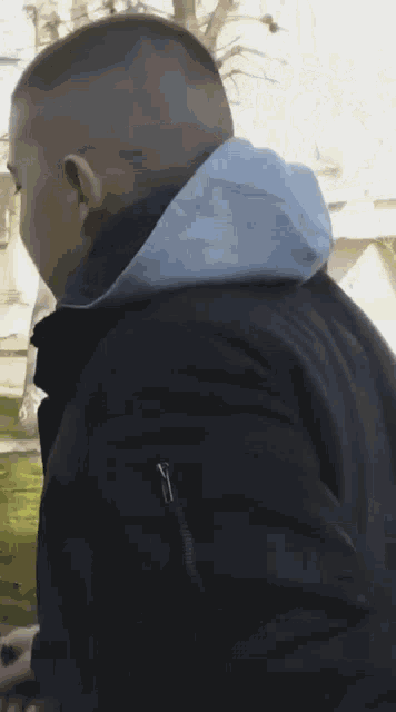 a man wearing a black jacket and a blue hoodie is standing in a park .