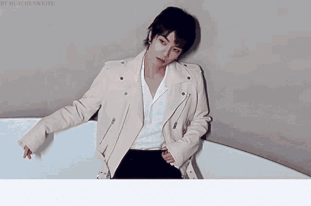 a woman wearing a white jacket and a white shirt is leaning on a wall
