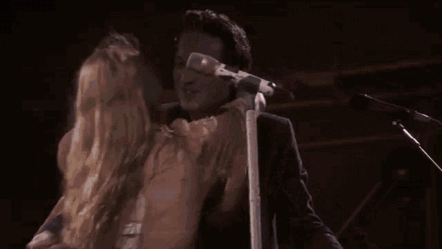 a man and a woman are hugging each other on a stage while a man sings into a microphone .