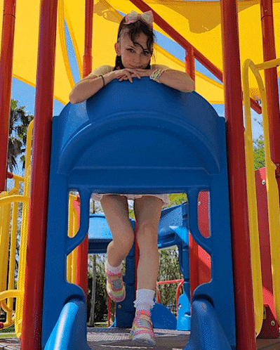a little girl is sitting on a slide at a playground