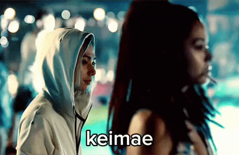 a woman in a hooded sweatshirt is standing next to another woman who is smoking a cigarette .