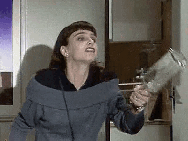 a woman in a blue sweater is holding a pitcher in front of a refrigerator door .