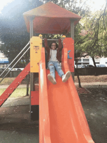 a little girl is sliding down an orange slide in a playground