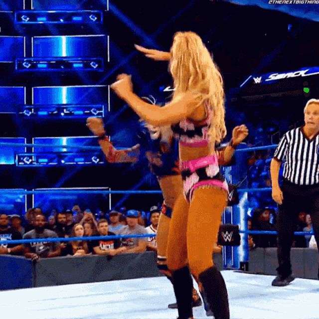 a woman is dancing in a wrestling ring while a referee stands behind her .