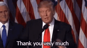 a man in a suit and tie is giving a speech in front of an american flag and saying `` thank you very much '' .