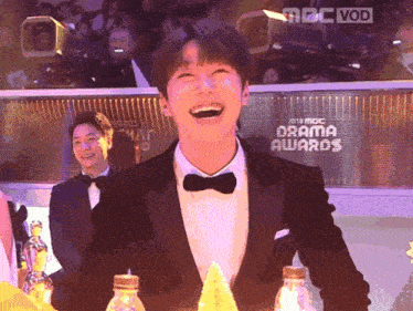 a man in a tuxedo is laughing in front of a screen that says drama awards