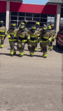 a group of firefighters are dancing in front of a red building