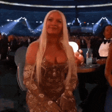 a woman with long blonde hair is sitting in front of a crowd at an event .