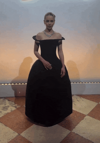 a woman in a black dress is standing in front of a wall