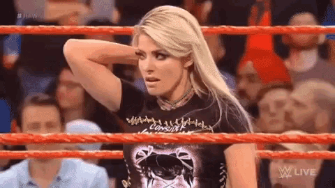 a woman in a black shirt is standing in a wrestling ring with her hand on her head .