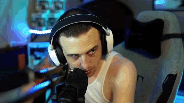 a man wearing headphones and a white tank top is sitting in front of a microphone
