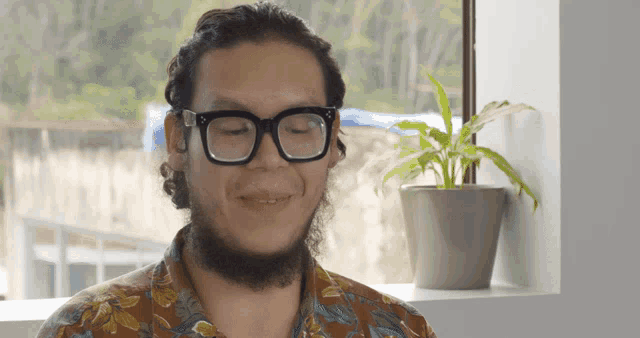 a man with glasses and a beard is smiling in front of a potted plant