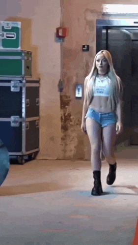 a woman in a crop top and shorts is walking down a hallway