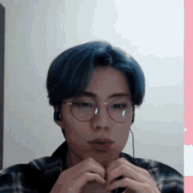 a man with blue hair and glasses is making a heart shape with his hands .