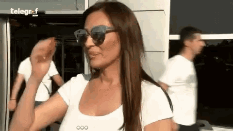 a woman wearing sunglasses and a white shirt is waving