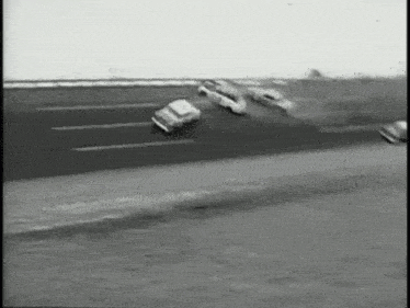 a black and white photo of cars racing on a track