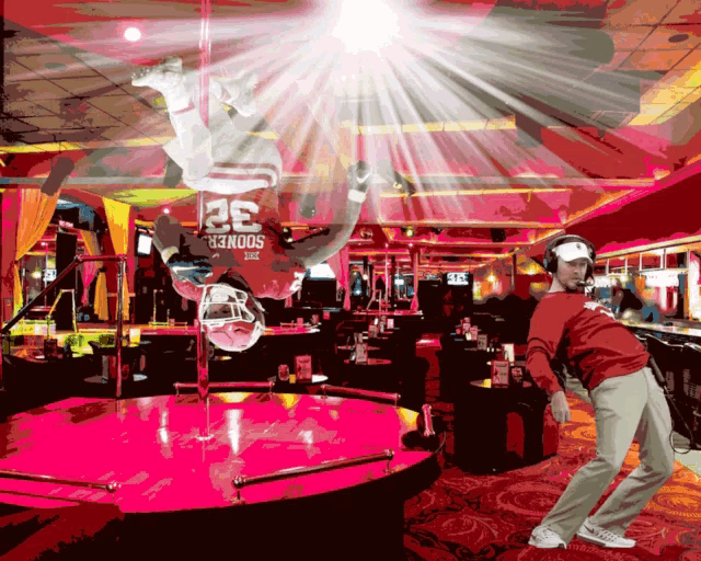 a man wearing headphones stands in front of a pole dancer wearing a sooners jersey