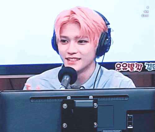 a man with pink hair is wearing headphones and sitting in front of a monitor .