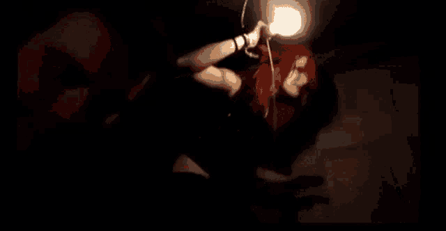 a woman with red hair is holding a light bulb in her hand in the dark