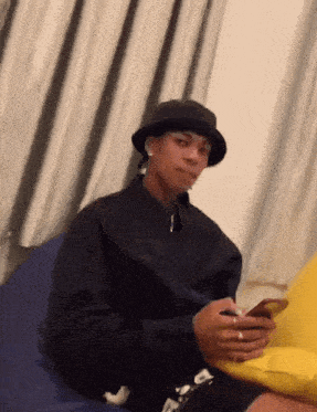a man wearing a black hat is sitting on a bean bag chair looking at his cell phone