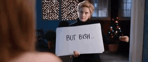a woman is holding a sign that says `` but ish '' in front of a christmas tree .