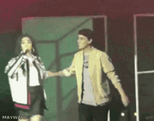 a man and a woman holding hands on a stage with mayward written on the bottom left