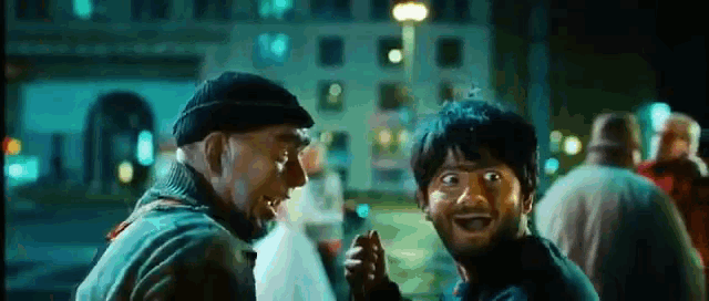 two men are standing next to each other in a crowded street at night making funny faces .