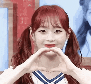 a girl with pigtails is making a heart shape with her hands .