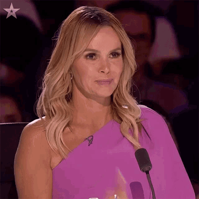 a woman in a purple one shoulder dress is sitting in front of a microphone