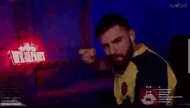 a man with a beard is sitting in front of a computer screen with a red light behind him .