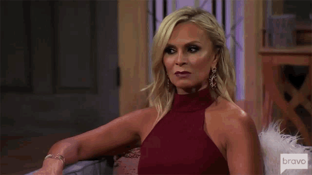 a woman in a red dress is sitting on a couch and making a funny face .