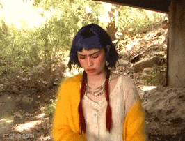 a girl with blue hair and red braids is wearing a yellow sweater and a white shirt .