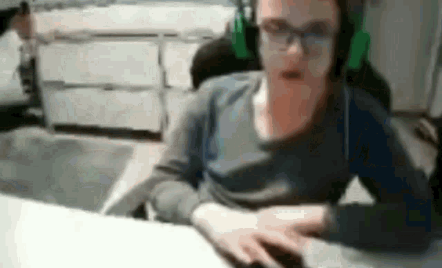 a man wearing headphones and glasses is sitting at a desk with a computer mouse .