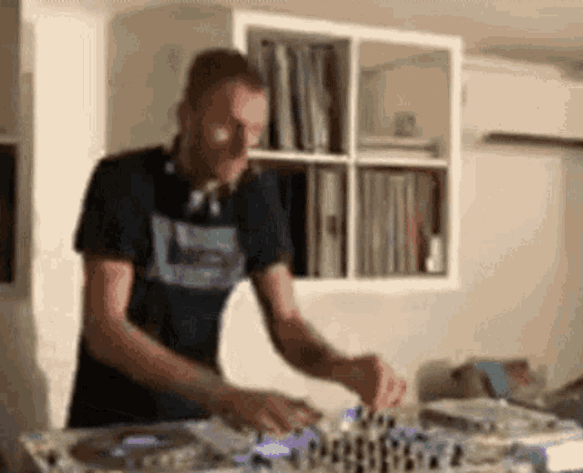 a man in a black shirt is playing a dj set in a room .