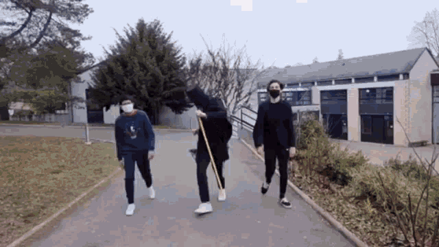 three people are walking down a sidewalk wearing masks and holding sticks .