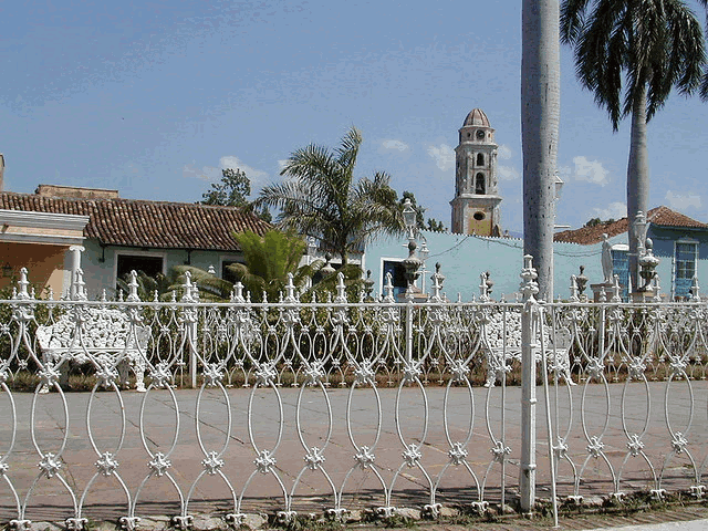 a white wrought iron fence surrounds a street with a church tower in the background