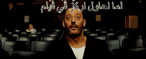 a man with a beard is sitting in an auditorium with arabic writing on it