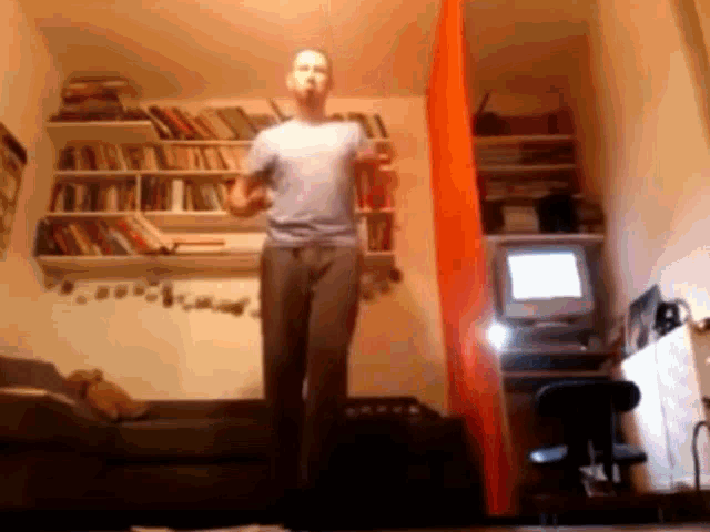 a man is dancing in a living room in front of a computer monitor