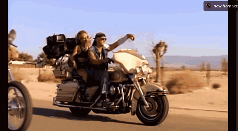 a couple riding a harley davidson motorcycle with a now from sts button